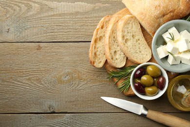 Photo of Delicious marinated olives, bread and feta cheese served on wooden table, top view. Space for text