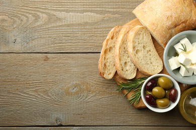 Photo of Delicious marinated olives, bread and feta cheese served on wooden table, top view. Space for text