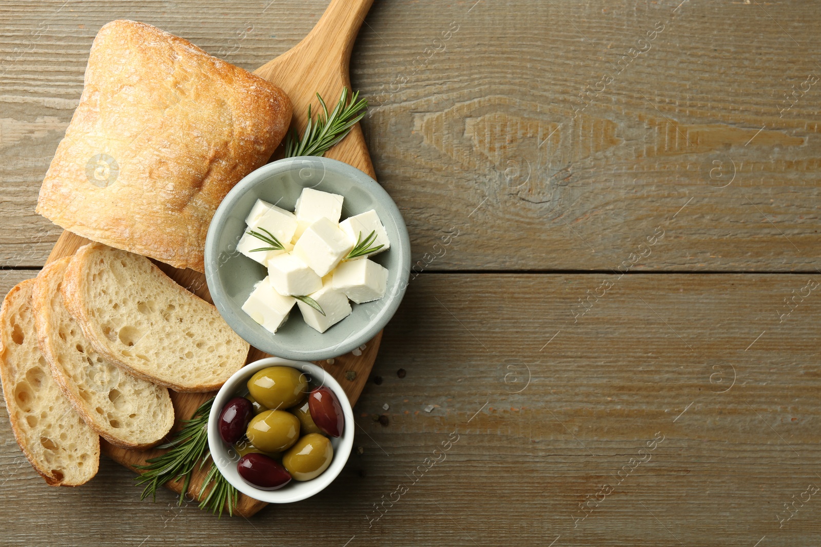 Photo of Delicious marinated olives, bread and feta cheese served on wooden table, top view. Space for text