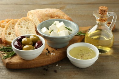 Photo of Delicious marinated olives, bread and feta cheese served on wooden table