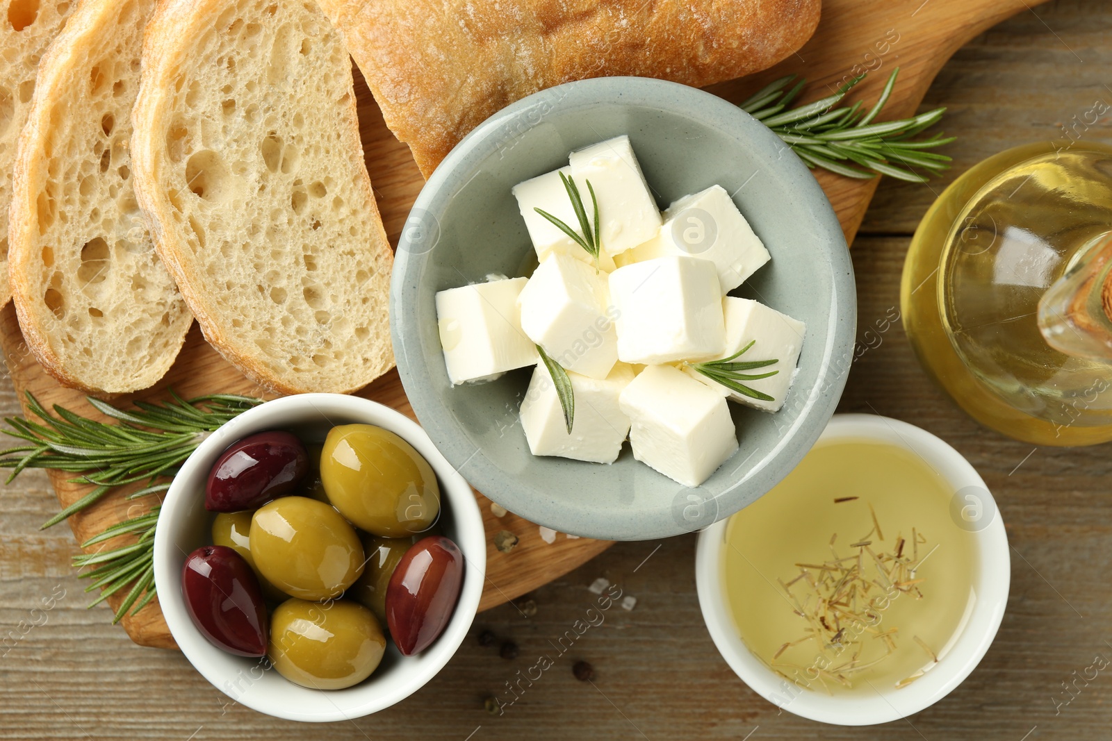 Photo of Delicious marinated olives, bread and feta cheese served on wooden table, flat lay