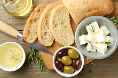 Photo of Delicious marinated olives, bread and feta cheese served on wooden table, flat lay