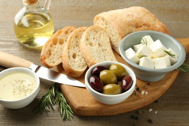 Photo of Delicious marinated olives, bread and feta cheese served on wooden table, closeup