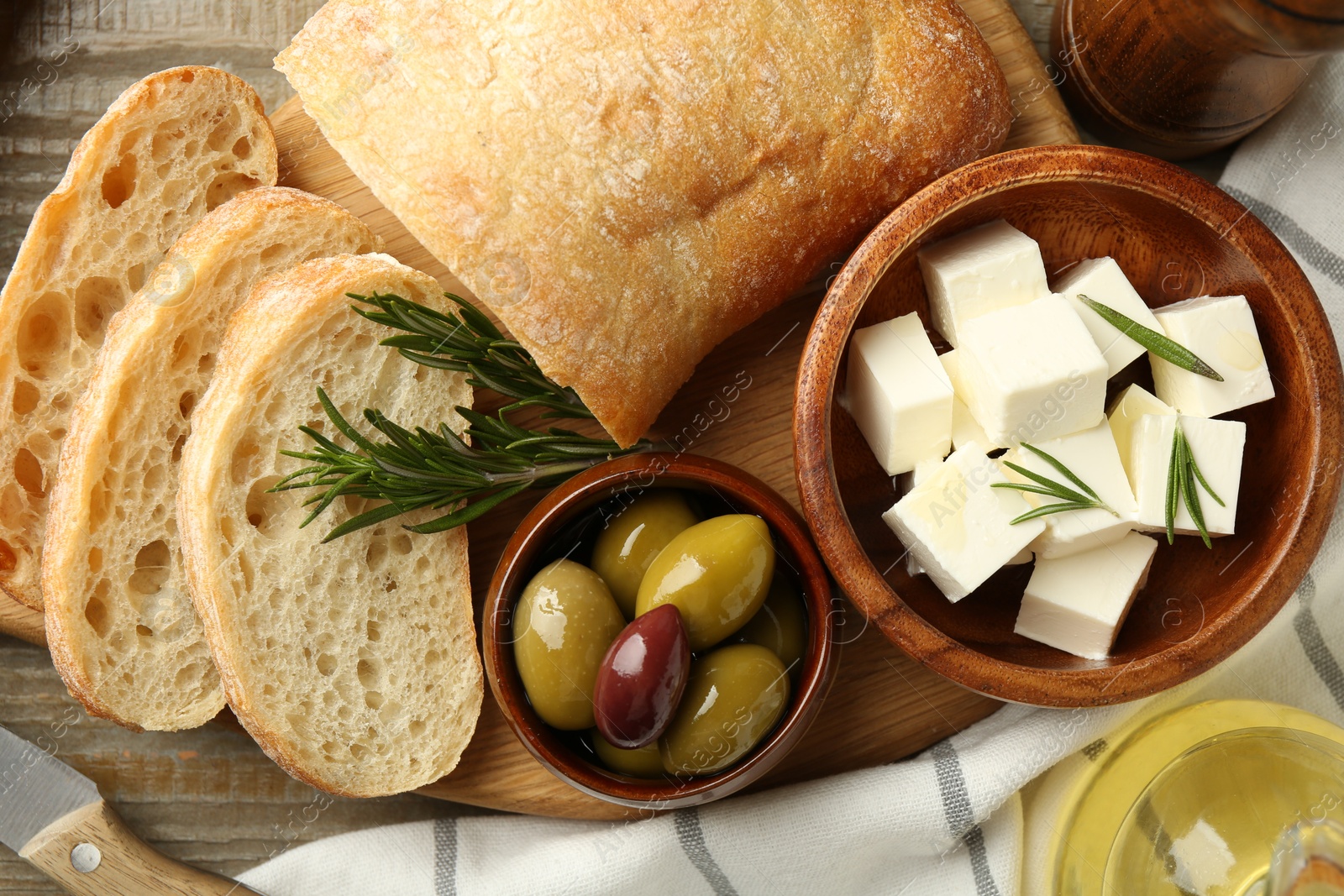 Photo of Delicious marinated olives, bread and feta cheese served on wooden table, flat lay