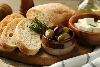 Photo of Delicious marinated olives, bread and feta cheese served on wooden table, closeup