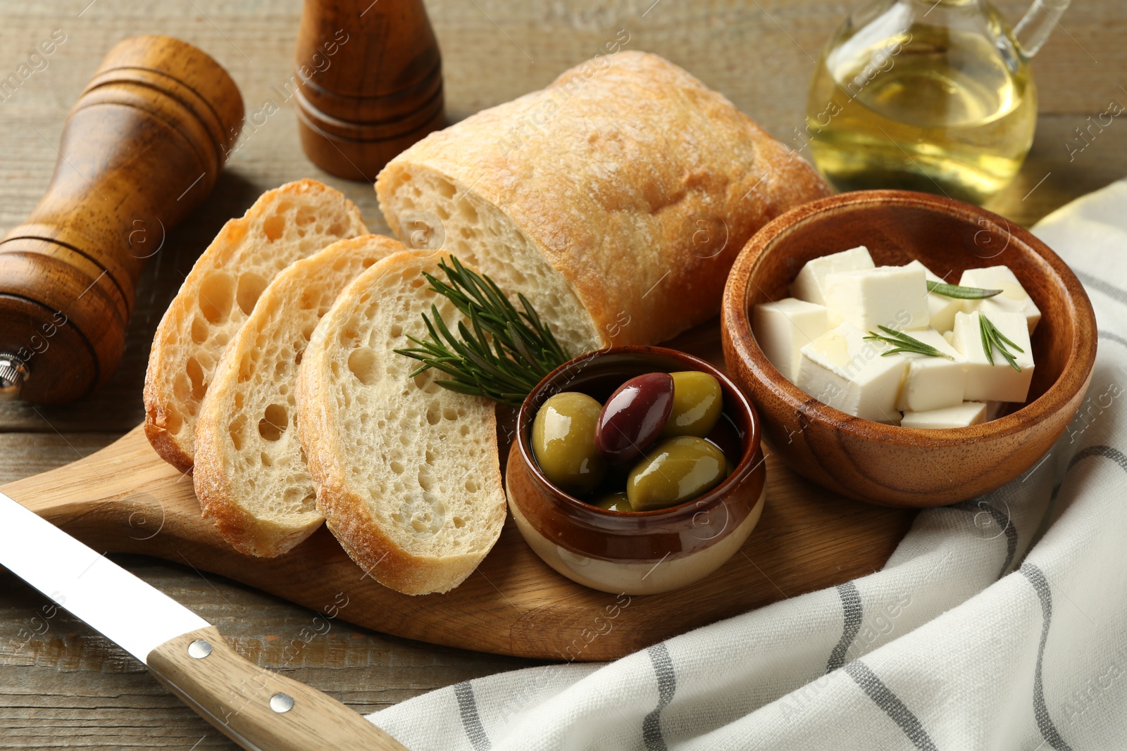 Photo of Delicious marinated olives, bread and feta cheese served on wooden table, closeup