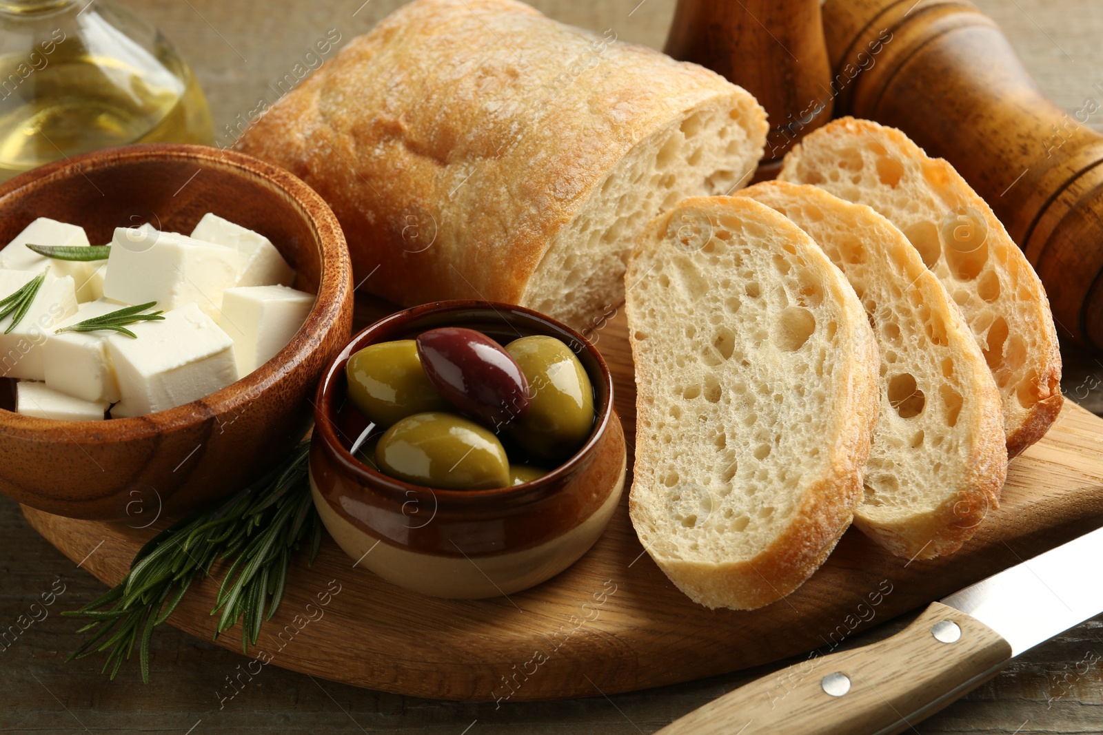 Photo of Delicious marinated olives, bread and feta cheese served on wooden table, closeup