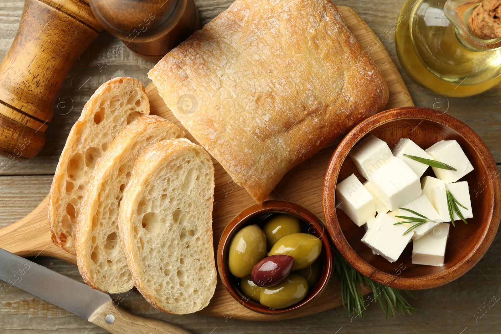 Photo of Delicious marinated olives, bread and feta cheese served on wooden table, flat lay