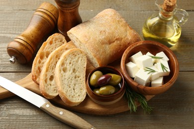 Photo of Delicious marinated olives, bread and feta cheese served on wooden table, closeup