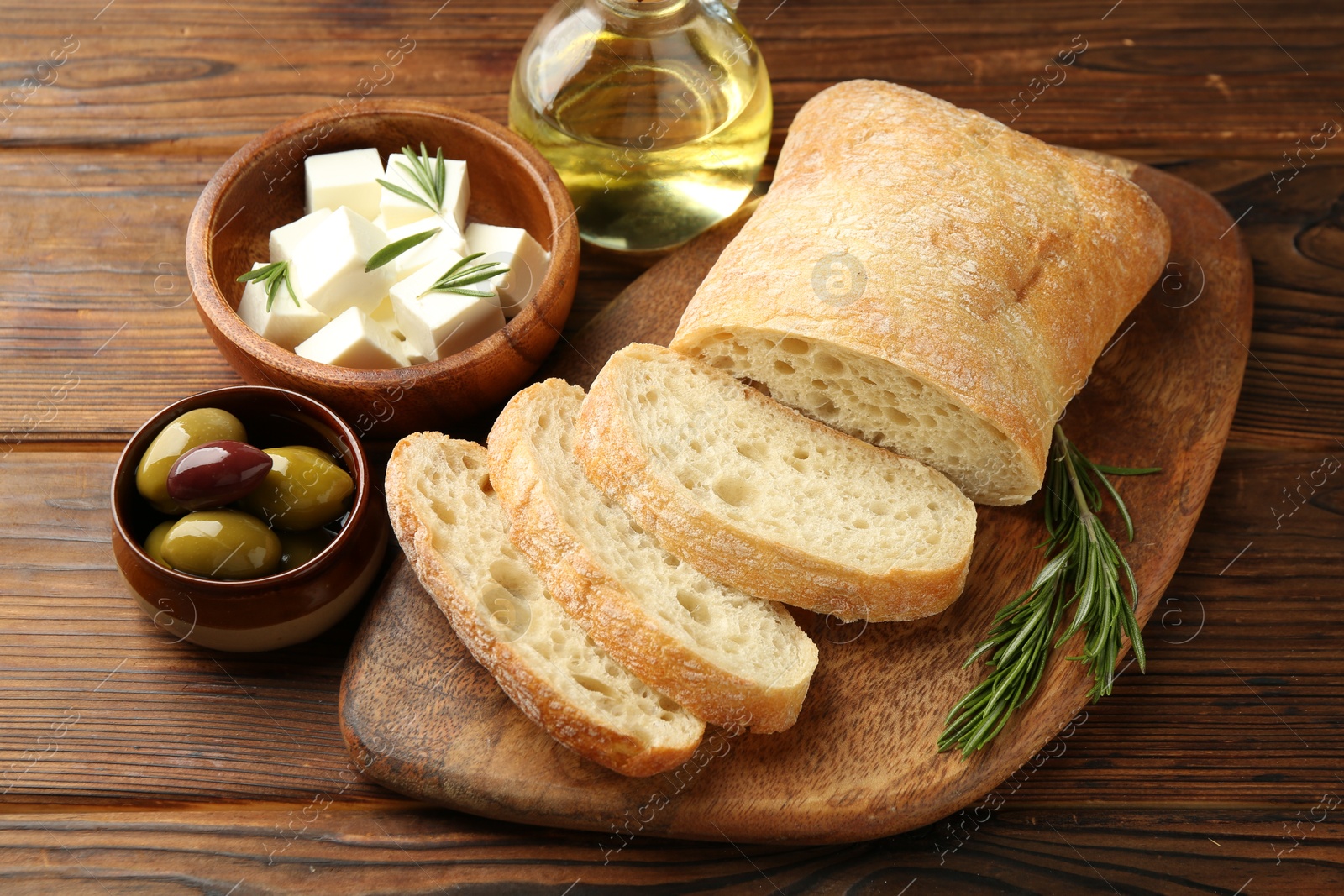 Photo of Delicious marinated olives, bread and feta cheese served on wooden table, closeup