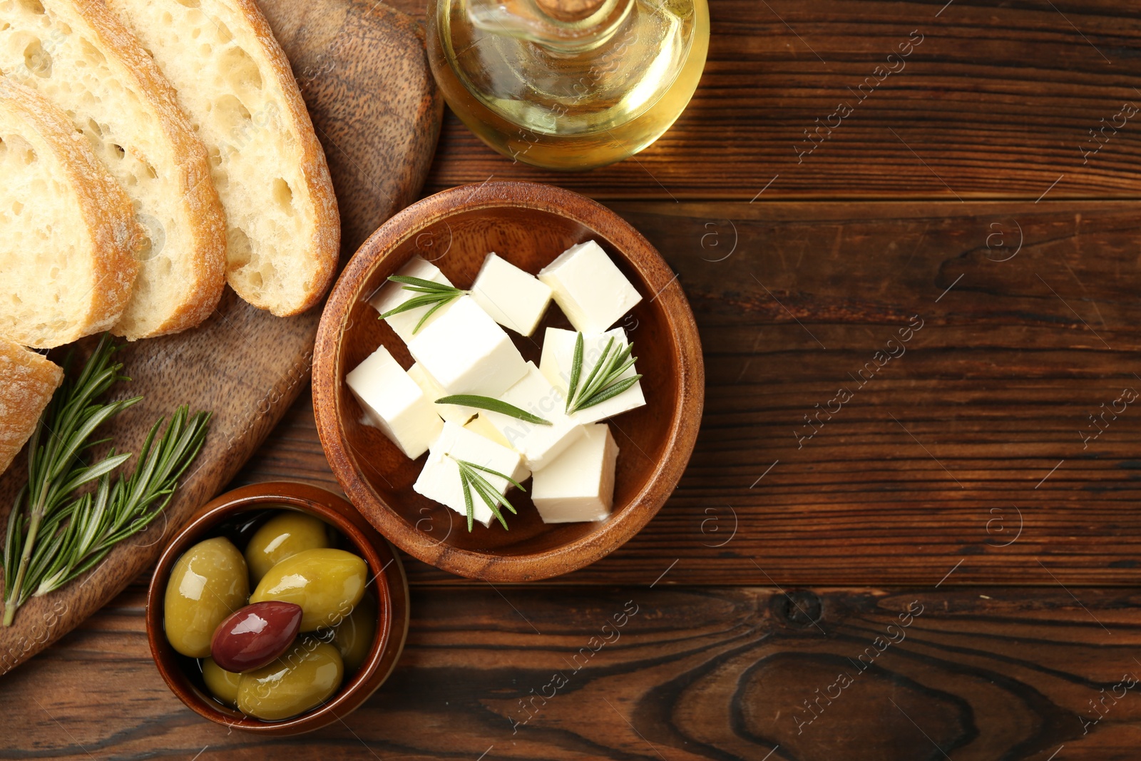 Photo of Delicious marinated olives, bread and feta cheese served on wooden table, top view. Space for text