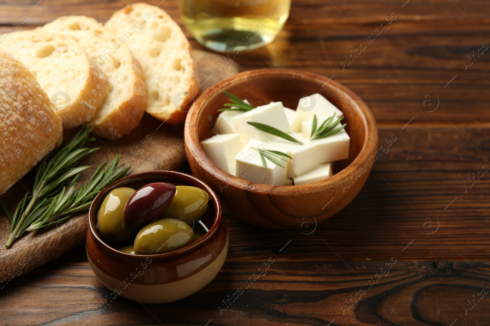 Photo of Delicious marinated olives, bread and feta cheese served on wooden table, closeup