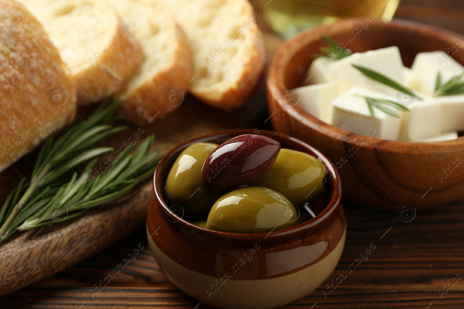 Photo of Delicious marinated olives, bread and feta cheese served on wooden table, closeup