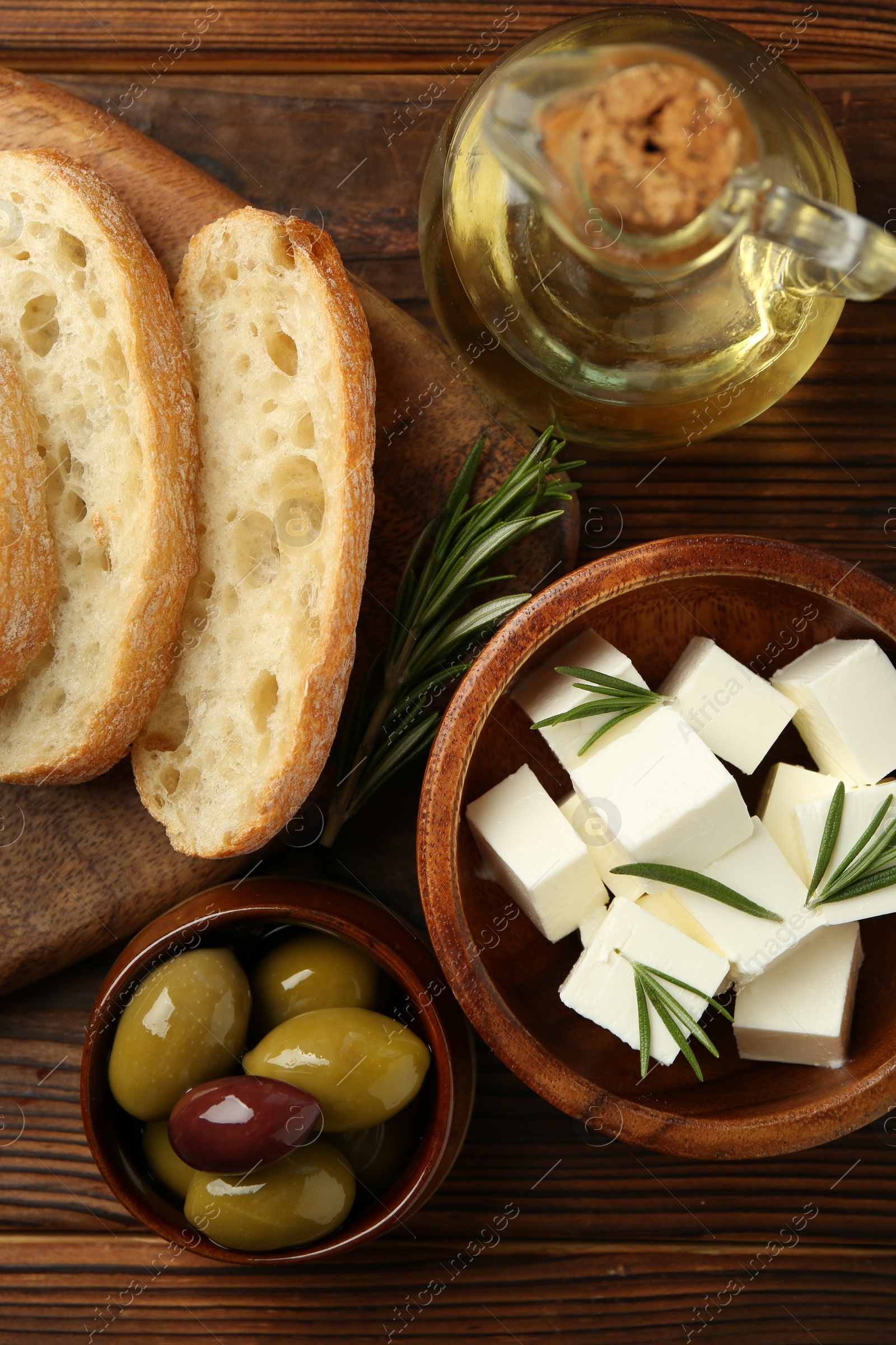 Photo of Delicious marinated olives, bread and feta cheese served on wooden table, flat lay