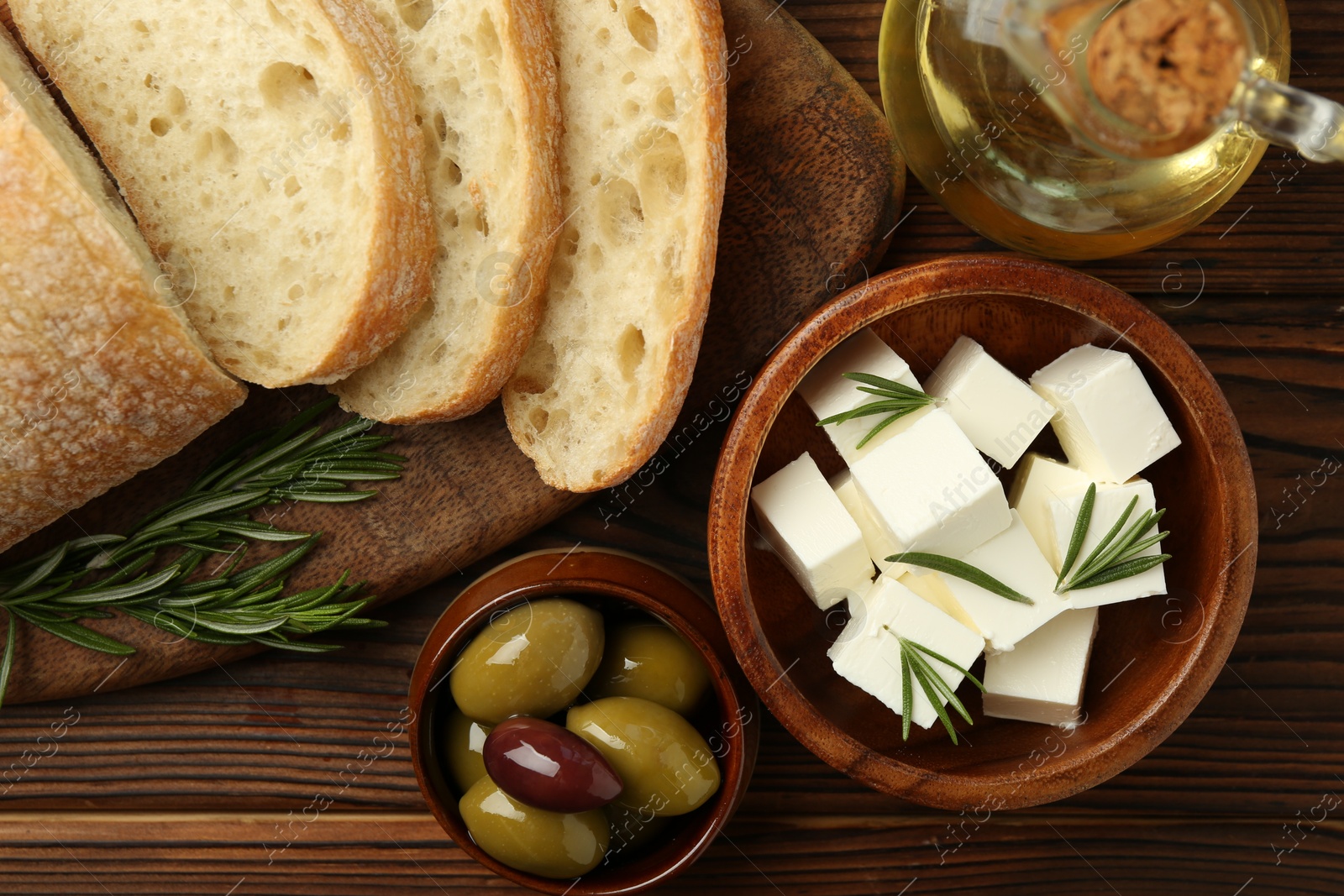 Photo of Delicious marinated olives, bread and feta cheese served on wooden table, flat lay