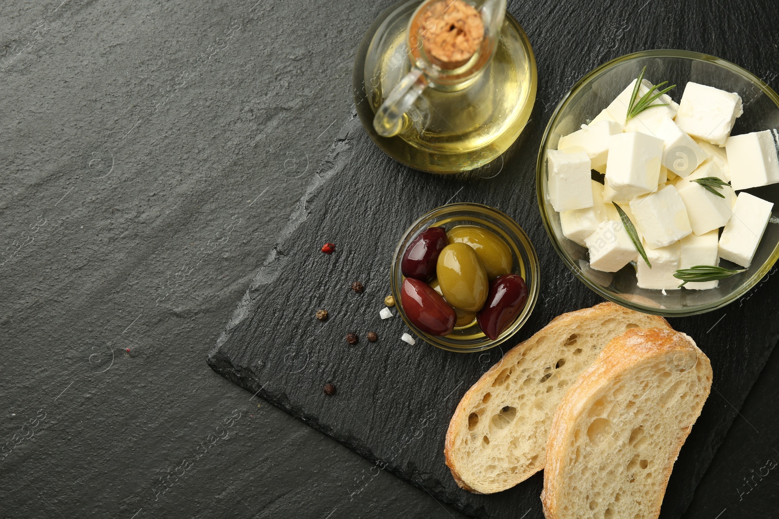 Photo of Delicious marinated olives, bread and feta cheese served on black table, top view. Space for text