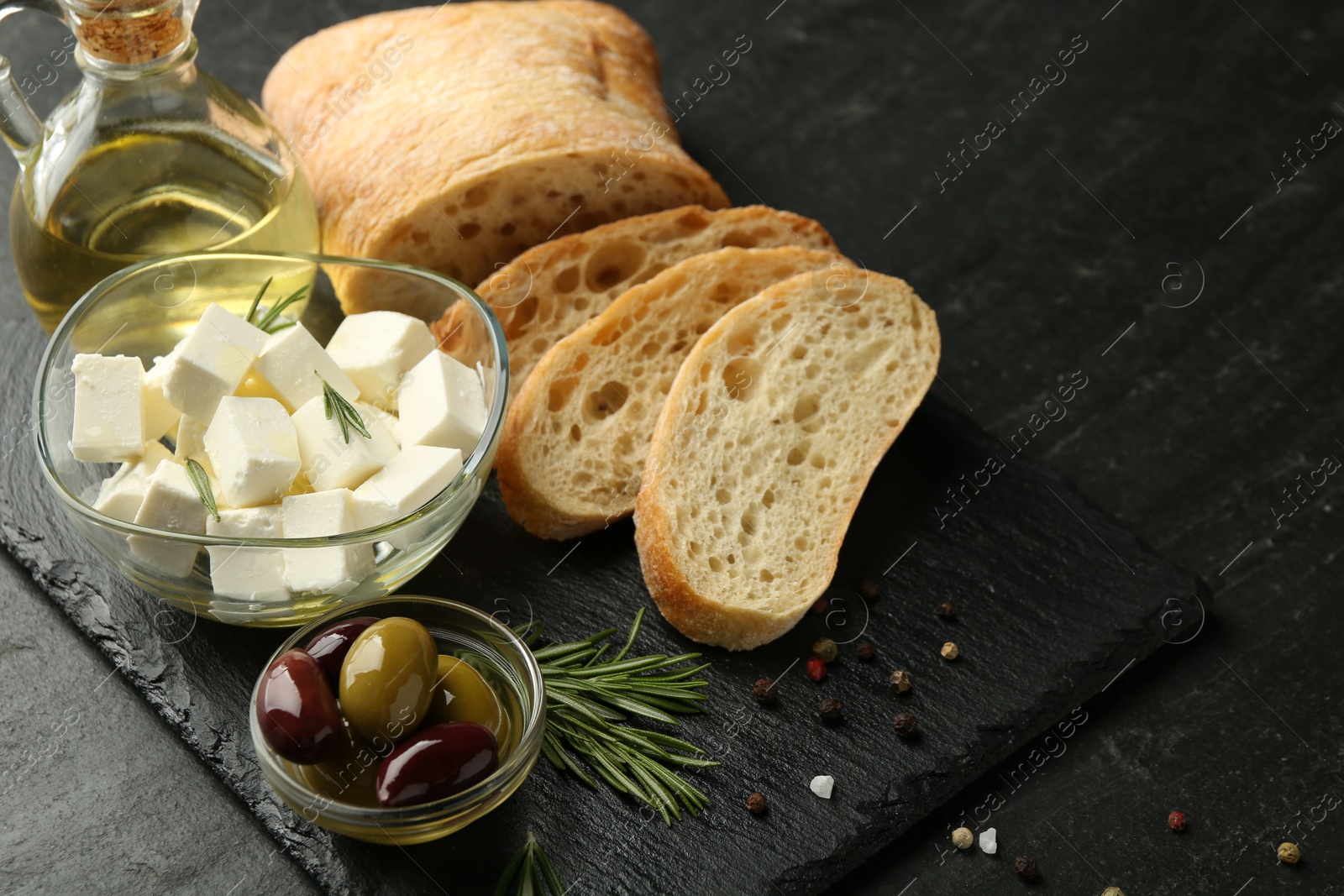 Photo of Delicious marinated olives, bread and feta cheese served on black table, closeup