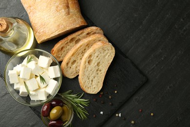 Photo of Delicious marinated olives, bread and feta cheese served on black table, top view. Space for text