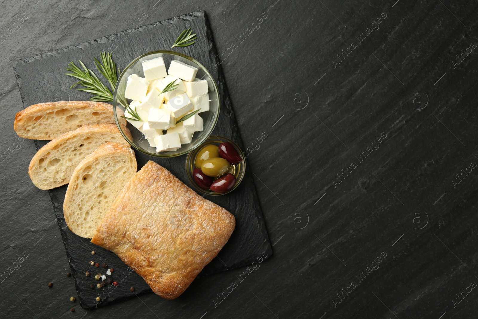 Photo of Delicious marinated olives, bread and feta cheese served on black table, top view. Space for text