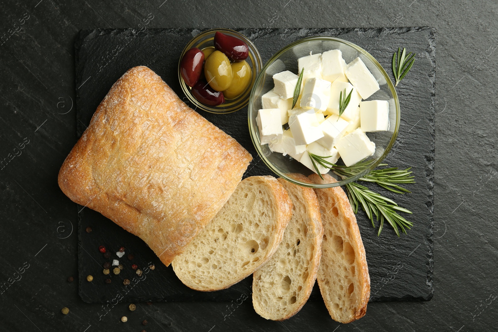 Photo of Delicious marinated olives, bread and feta cheese served on black table, top view