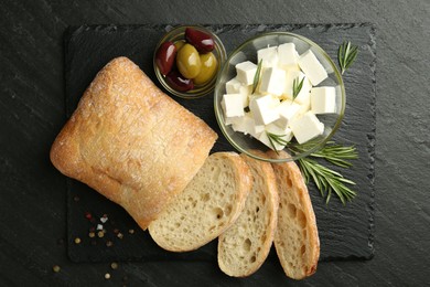 Photo of Delicious marinated olives, bread and feta cheese served on black table, top view