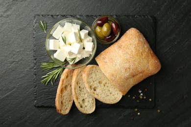 Photo of Delicious marinated olives, bread and feta cheese served on black table, top view