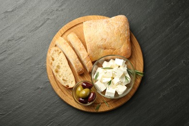 Photo of Delicious marinated olives, bread and feta cheese served on black table, top view