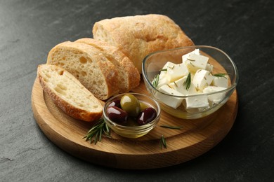 Photo of Delicious marinated olives, bread and feta cheese served on black table, closeup