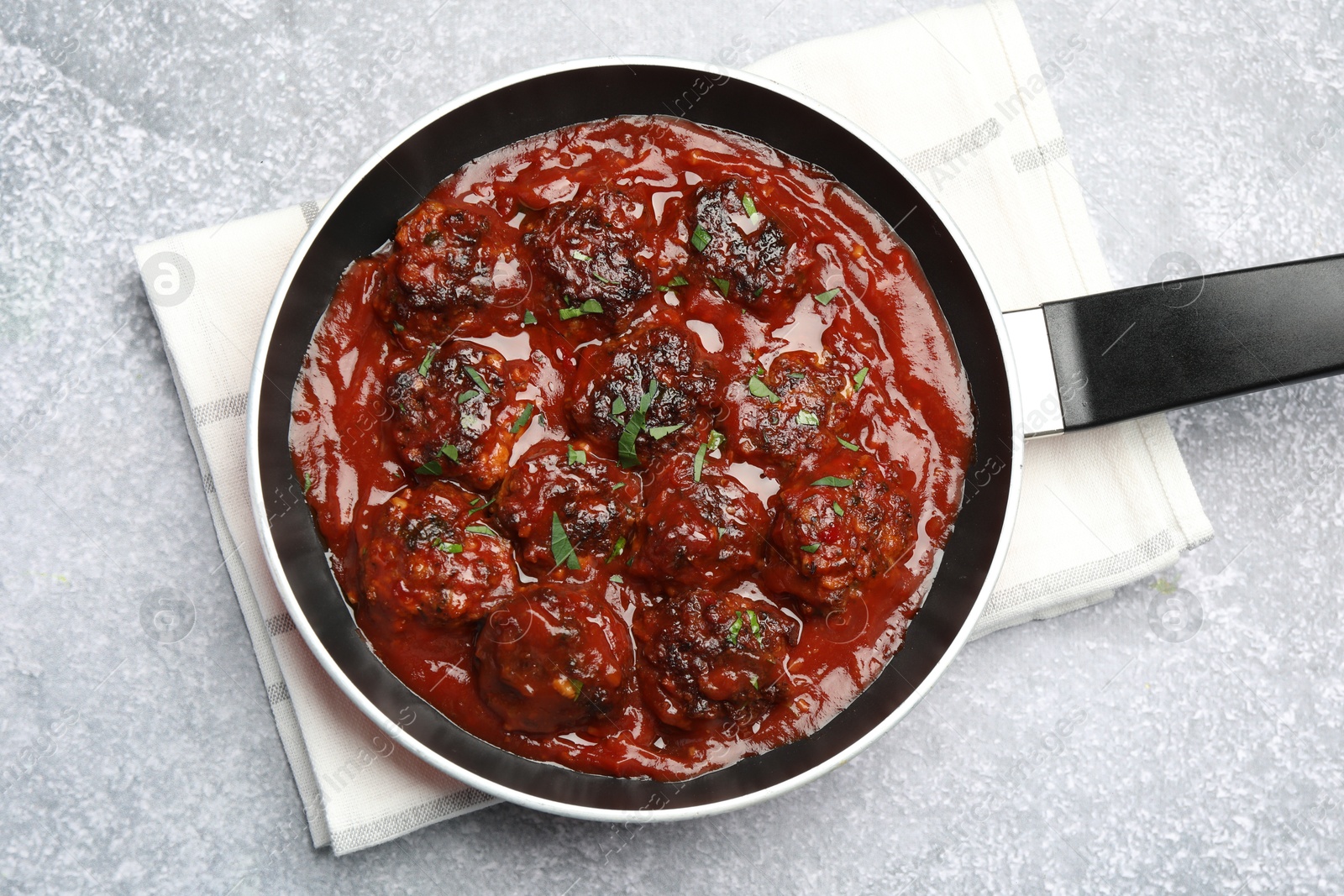 Photo of Delicious meatballs with tomato sauce and herbs in on grey table, top view