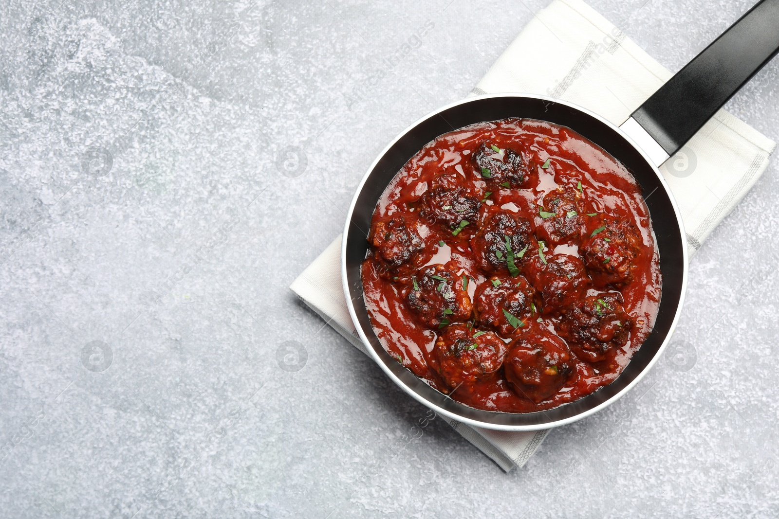 Photo of Delicious meatballs with tomato sauce and herbs in on grey table, top view. Space for text