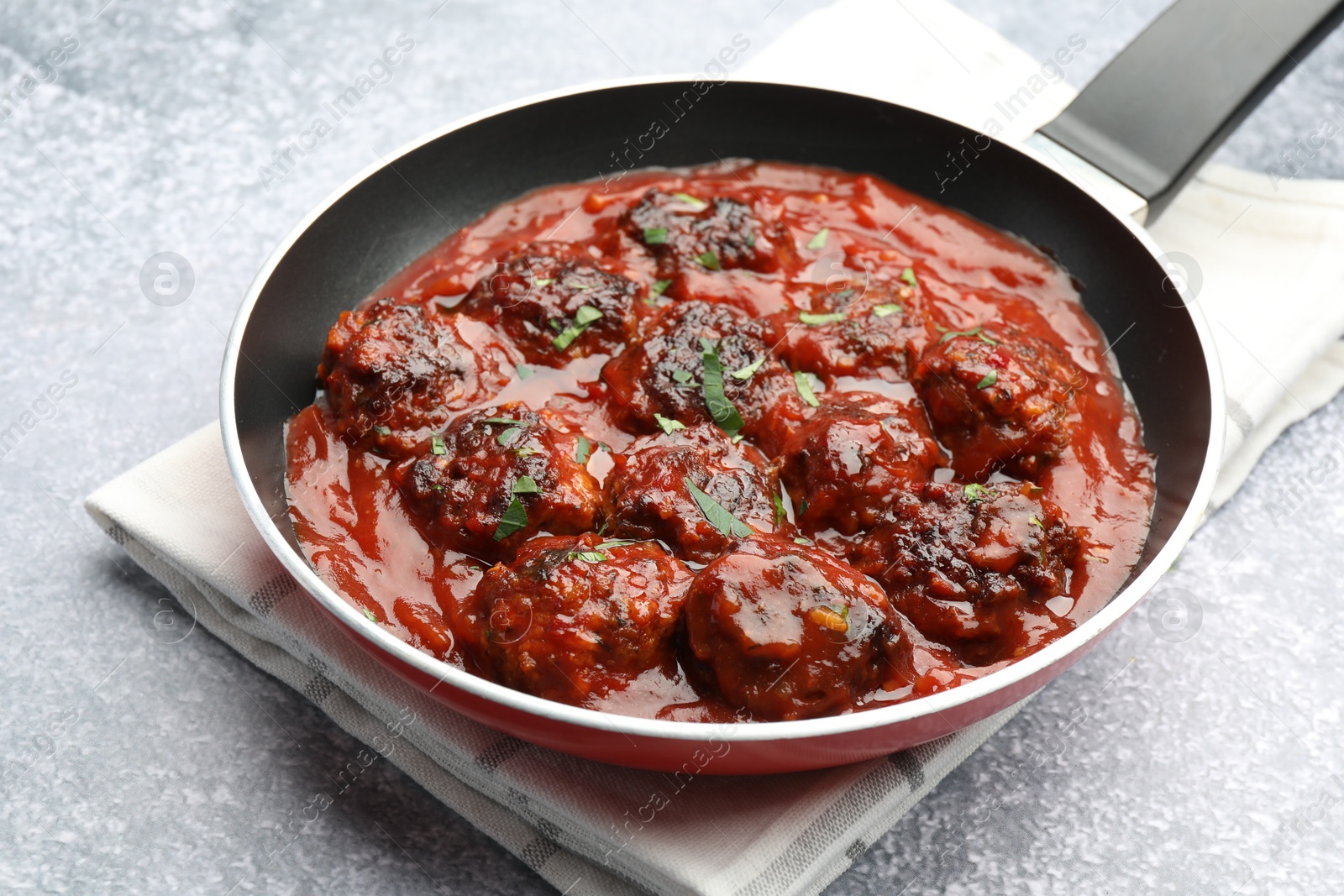 Photo of Delicious meatballs with tomato sauce and herbs in on grey table, closeup