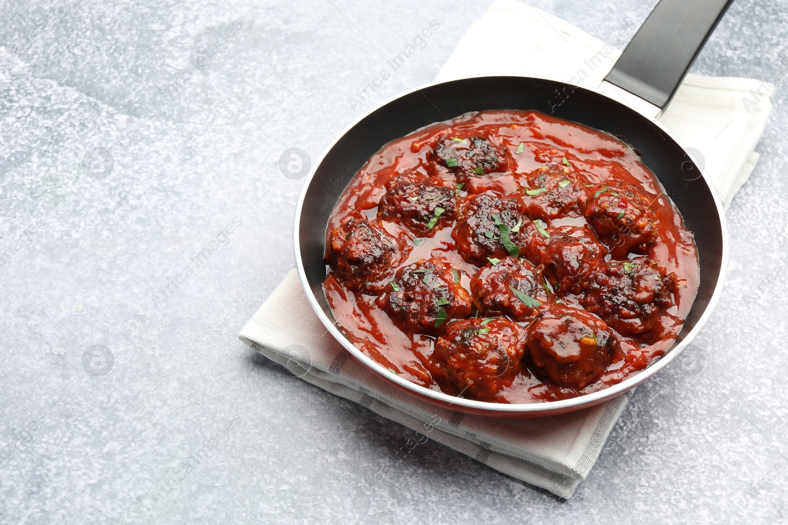 Photo of Delicious meatballs with tomato sauce and herbs in on grey table. Space for text