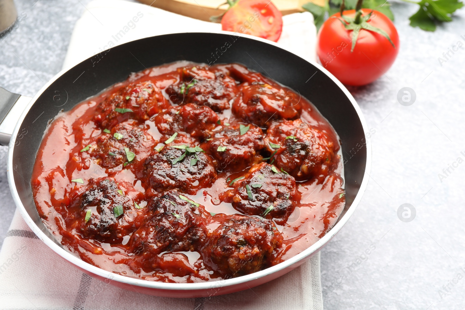 Photo of Delicious meatballs with tomato sauce and herbs in on grey table, closeup