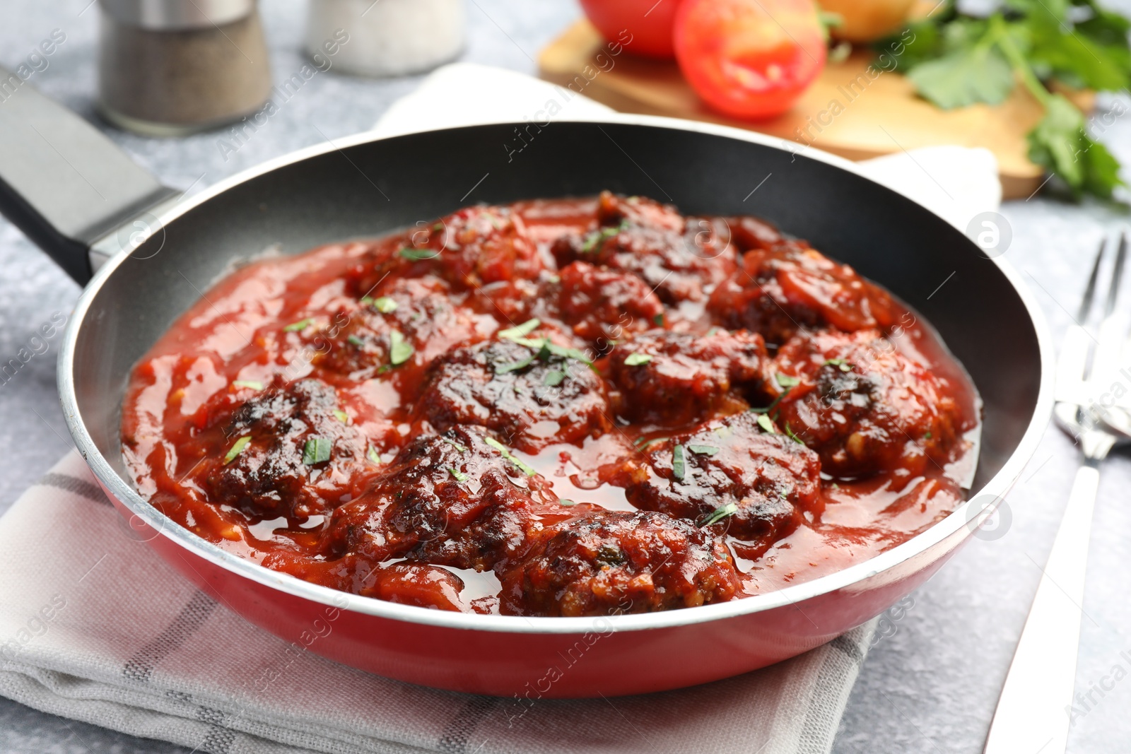 Photo of Delicious meatballs with tomato sauce and herbs in served on grey table, closeup