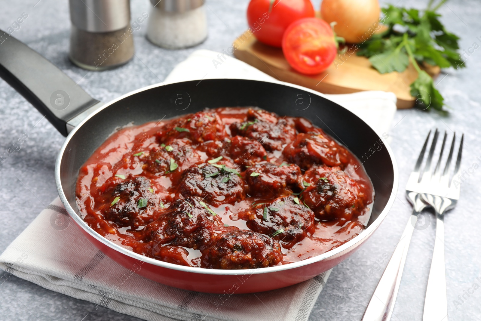 Photo of Delicious meatballs with tomato sauce and herbs in served on grey table