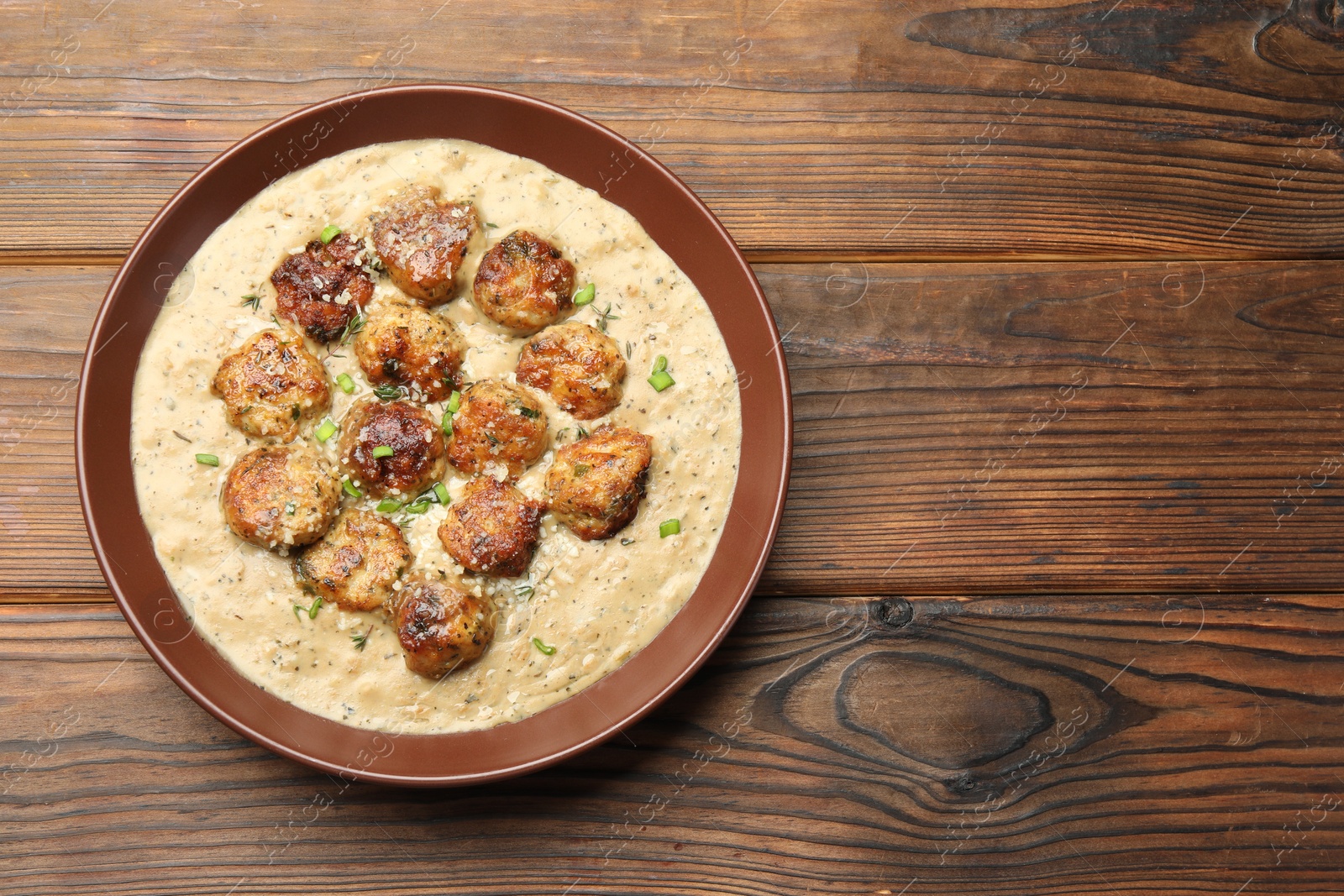 Photo of Delicious meatballs with gravy cream sauce and herbs on wooden table, top view. Space for text