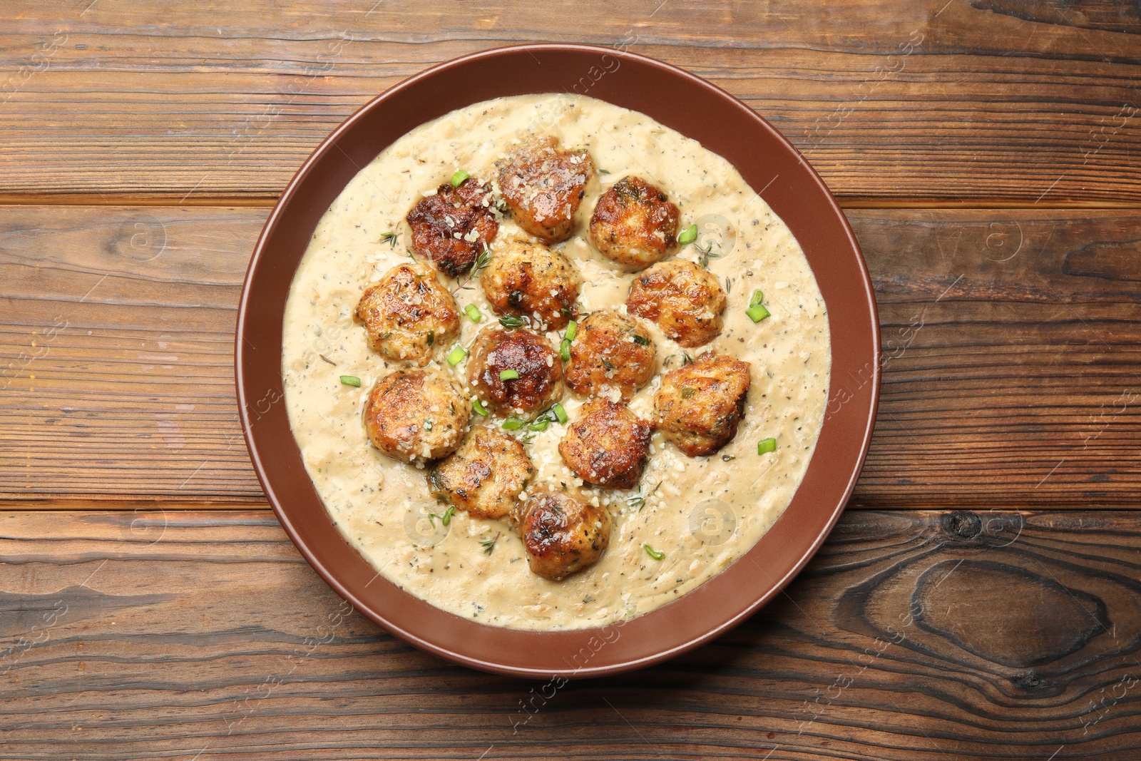 Photo of Delicious meatballs with gravy cream sauce and herbs on wooden table, top view