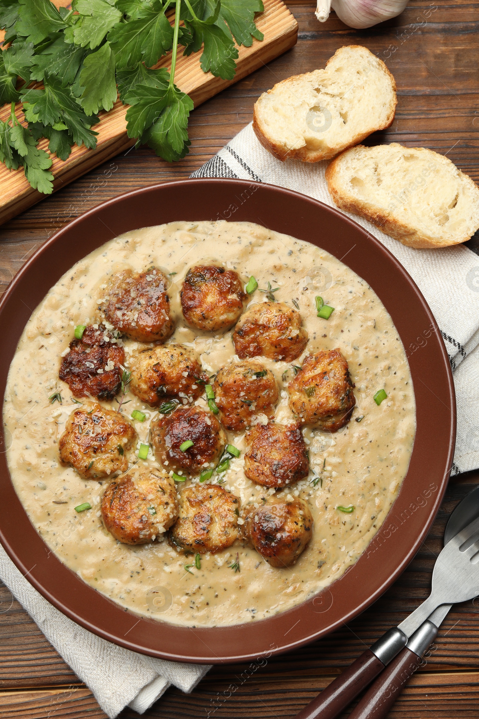 Photo of Delicious meatballs with gravy cream sauce and herbs served on wooden table, flat lay