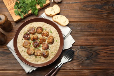 Photo of Delicious meatballs with gravy cream sauce and herbs served on wooden table, flat lay. Space for text