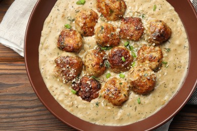 Photo of Delicious meatballs with gravy cream sauce and herbs on wooden table, top view