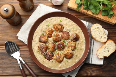 Photo of Delicious meatballs with gravy cream sauce and herbs served on wooden table, flat lay