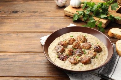 Photo of Delicious meatballs with gravy cream sauce and herbs served on wooden table. Space for text