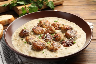 Photo of Delicious meatballs with gravy cream sauce and herbs served on wooden table, closeup