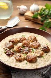 Photo of Delicious meatballs with gravy cream sauce and herbs served on wooden table, closeup