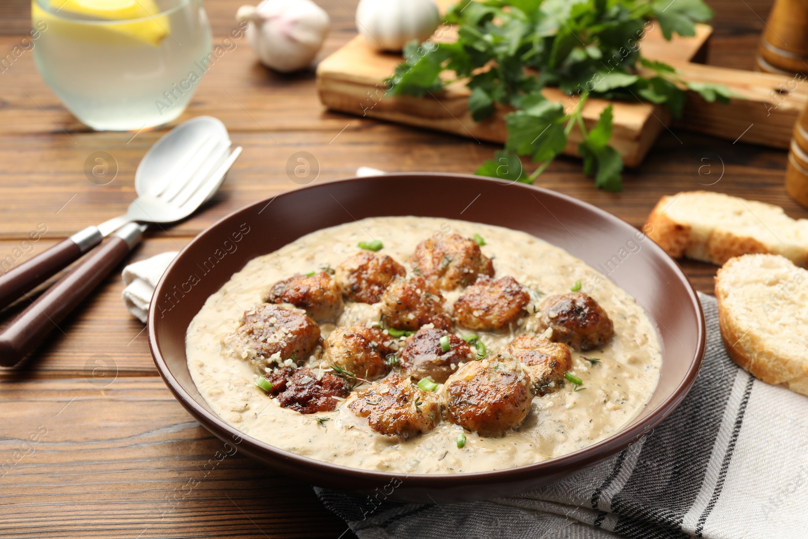 Photo of Delicious meatballs with gravy cream sauce and herbs served on wooden table