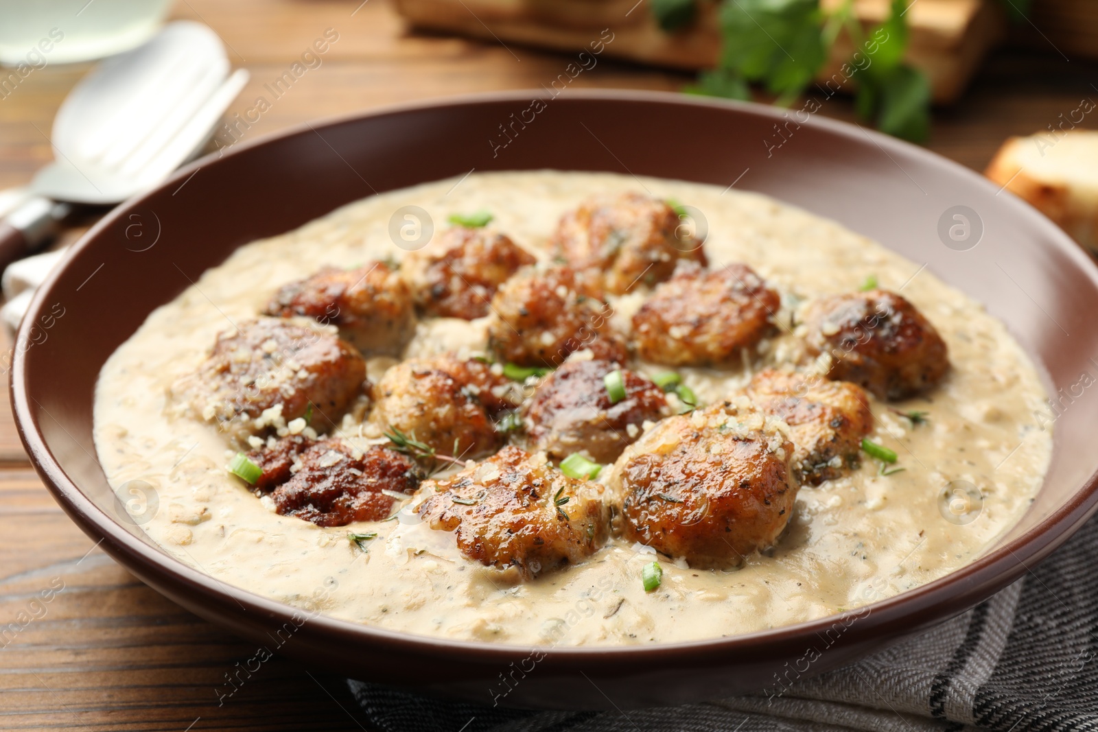 Photo of Delicious meatballs with gravy cream sauce and herbs served on wooden table, closeup