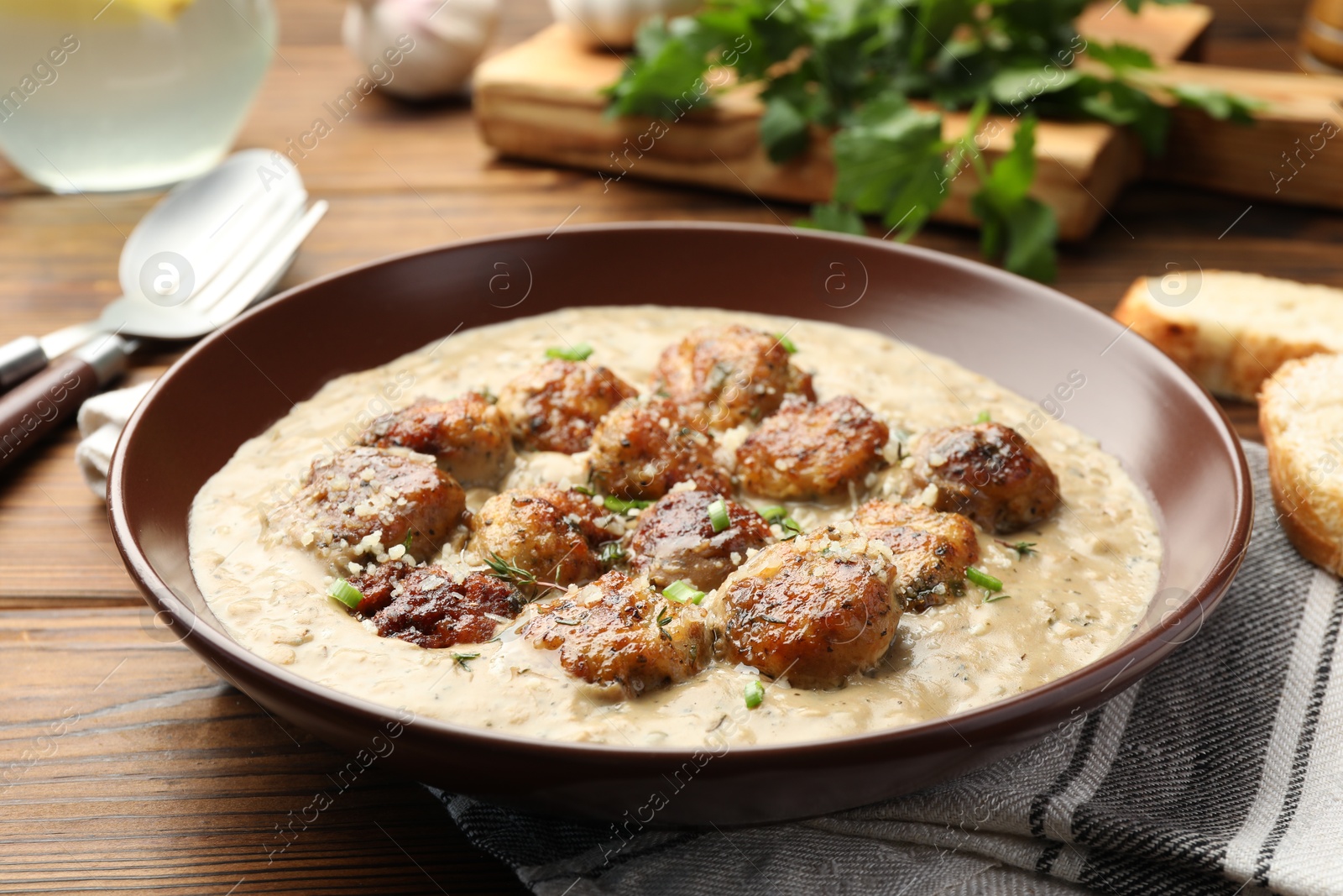 Photo of Delicious meatballs with gravy cream sauce and herbs served on wooden table, closeup