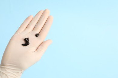 Photo of Woman holding medicinal leeches on light blue background, closeup. Space for text