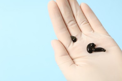 Photo of Woman holding medicinal leeches on light blue background, closeup. Space for text