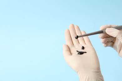 Photo of Woman holding medicinal leech with tweezers on light blue background, closeup. Space for text